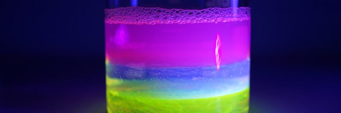 Vibrant layers of fluorescent liquids glowing in a lab beaker under UV light, showcasing scientific beauty.
